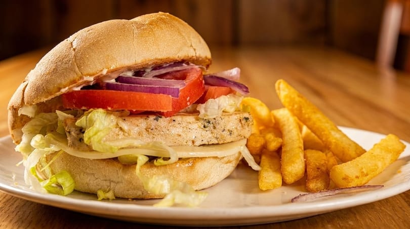 Chicken sandwich with lettuce, cheese, tomato, and red onion, served with golden fries.